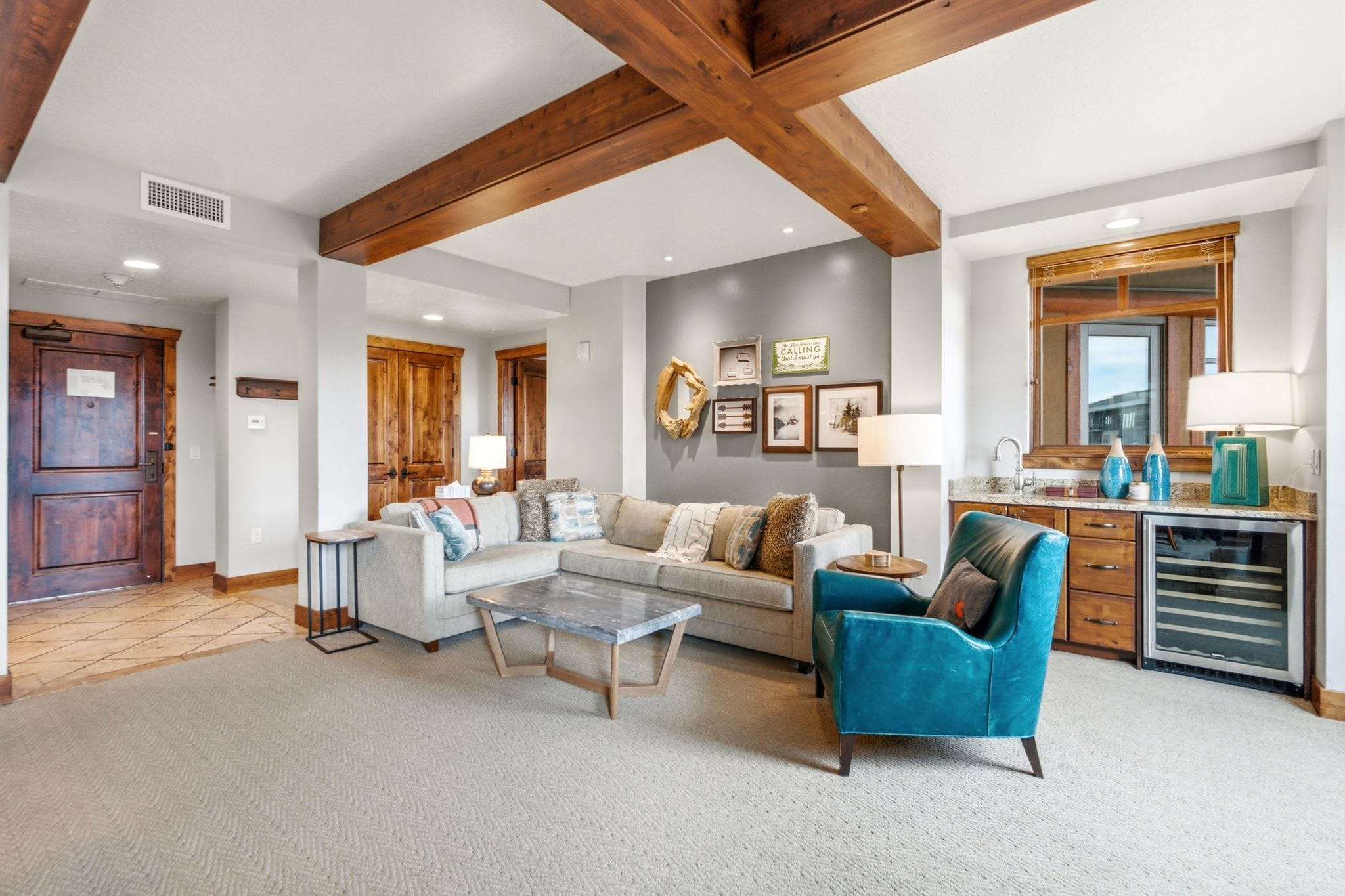 A spacious living room with a sofa, armchair, and coffee table, a kitchen area with a sink and cabinets, and a wooden ceiling.