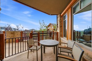 An outdoor patio with a round table and chairs, a stone wall, and a view of a mountain and buildings in the background. - Ski-in/Ski-out | Heated Pool, Hot Tubs & Game Room | Shuttle To Main St. (Park City)