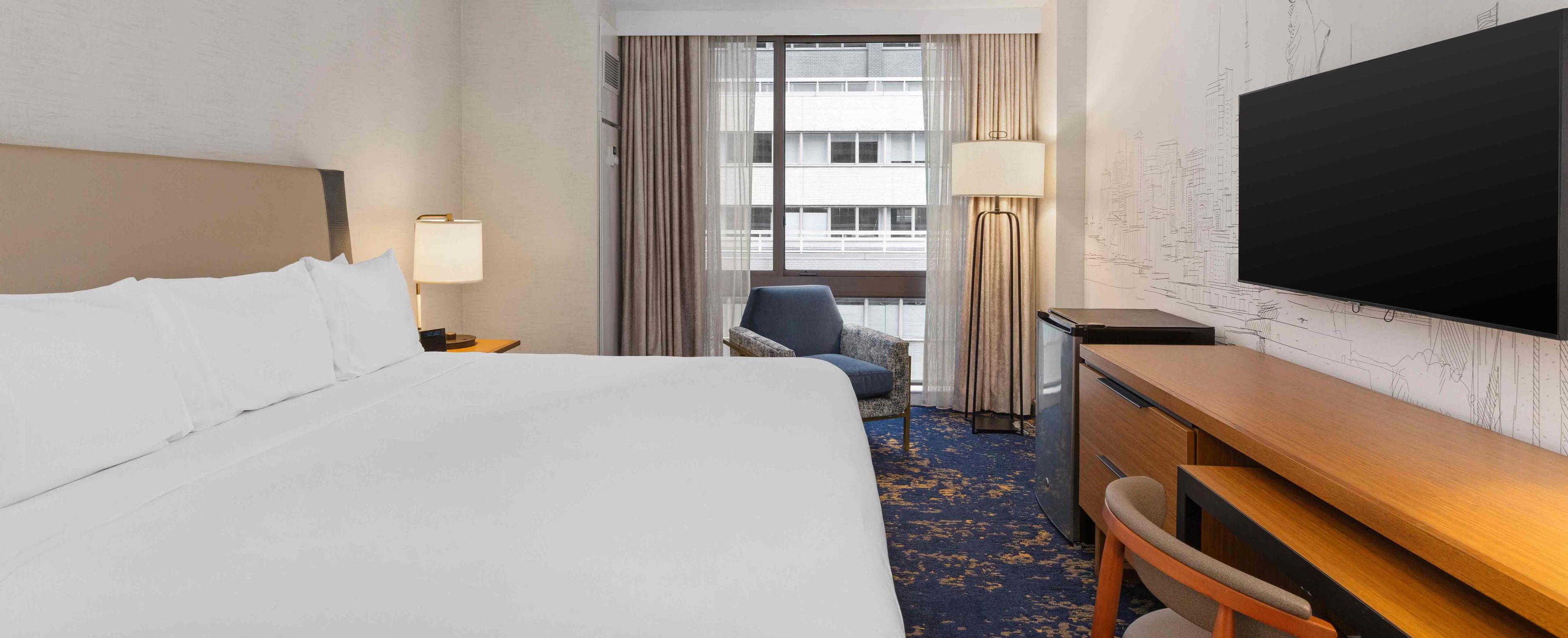 A hotel room with a bed, a desk, a chair, a television, and a window with curtains.