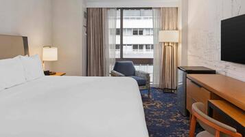 A hotel room with a bed, a desk, a chair, a television, and a window with curtains.