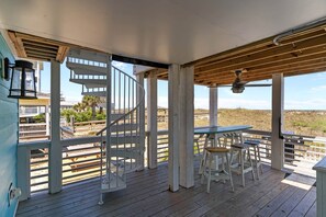 Eine Holzterrasse mit Wendeltreppe, Sitzgelegenheiten im Freien und Blick auf den Strand.