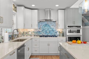 A modern kitchen with white cabinetry, a mosaic backsplash, and stainless steel appliances. - Sand By Me - oceanfront house with pool, elevator (Carolina Beach)