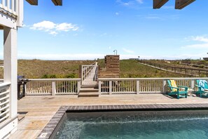 Ein Poolbereich mit Holzterrasse, Steinmauer und Blick auf den Strand.