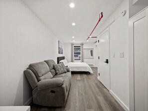 A modern bedroom with a sofa, a bed, and a view of the street. - Modern NYC King Room in Central Harlem (New York)