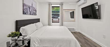 A modern hotel room with a bed, a bedside table with a plant, a TV mounted on the wall, and a cityscape painting.