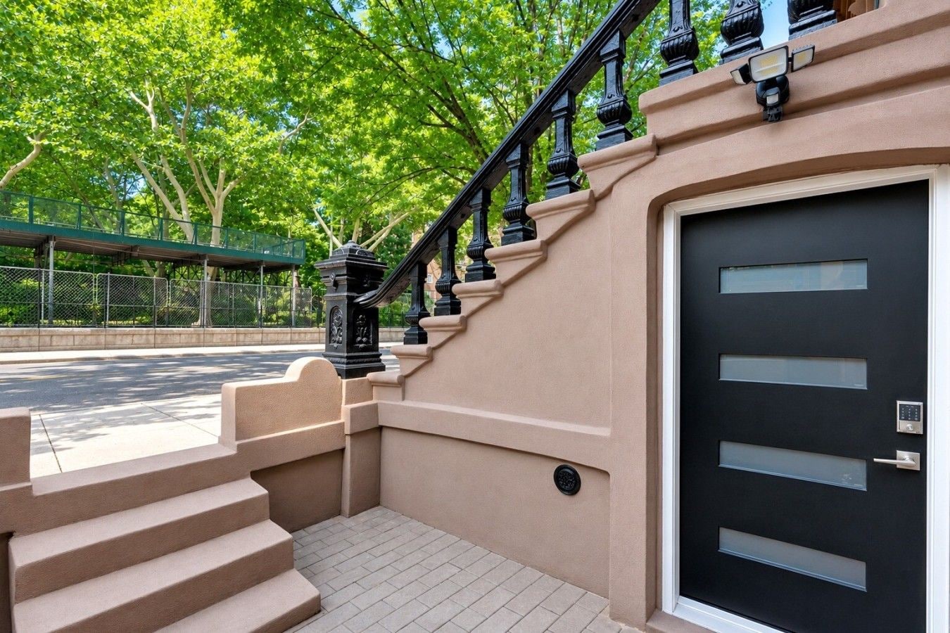 A residential building with a beige exterior, a black door with a keypad lock, and a staircase leading to the entrance.