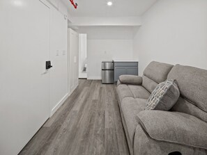 En modern inredning med en grå soffa, en papperskorg och en liten köksdel.