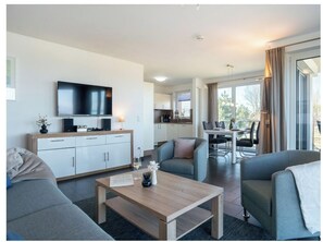 A modern hotel room with a flat-screen TV, a dining area, and a balcony with curtains. - Holiday Apartment With 1 Bedroom (Heiligenhafen)