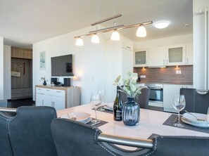 A modern kitchen with a dining area, including a table set for two with wine glasses and bottles. - Holiday Apartment With 1 Bedroom (Heiligenhafen)
