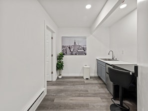 A narrow hallway leading to a kitchen with a cityscape view, a potted plant, and a trash bin. - Queen Room with Kitchenette in Central Harlem (New York)