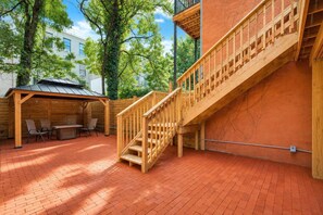 A wooden staircase leading to a covered outdoor area with a brick floor and a seating arrangement. - Modern Queen Room in Central Harlem (New York)
