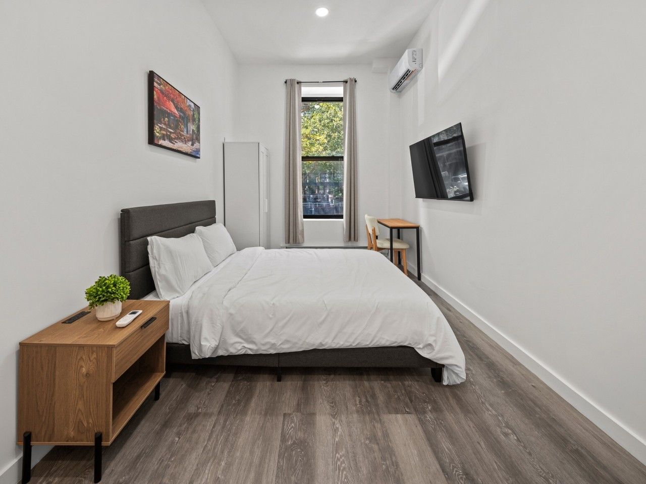 Quarto com cama, mesa de cabeceira e pequena mesa com uma planta.