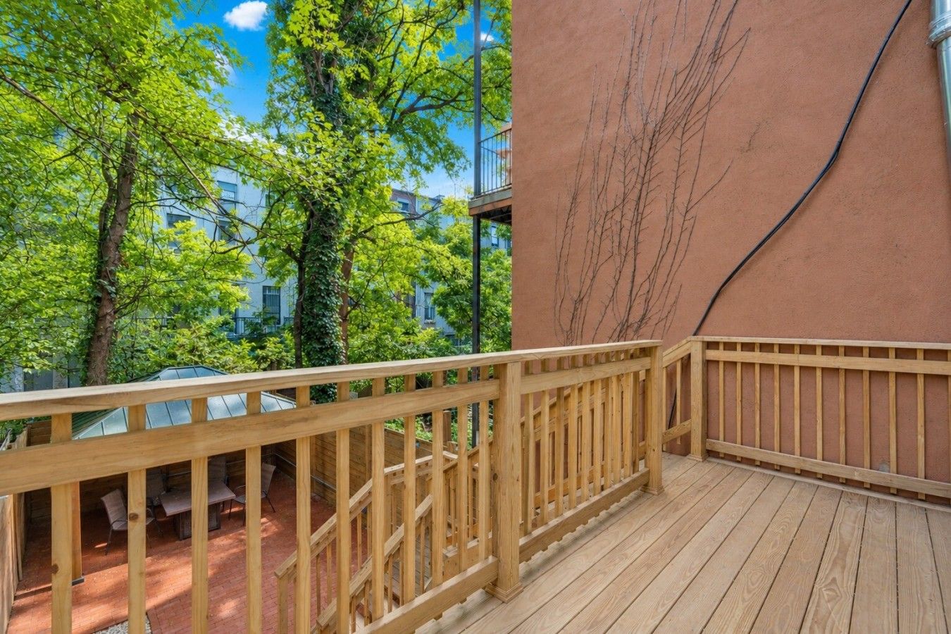 Une terrasse en bois, dotée d’une rambarde, qui donne sur une cour intérieure agrémentée d’arbres et bordée d’un bâtiment.