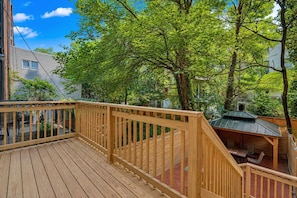 A wooden deck with a railing, surrounded by trees and a small building with a green roof. - King Studio with Kitchenette and Private Deck (New York)