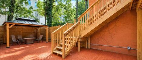 A wooden staircase leading to a covered outdoor area with a brick floor and a seating arrangement.