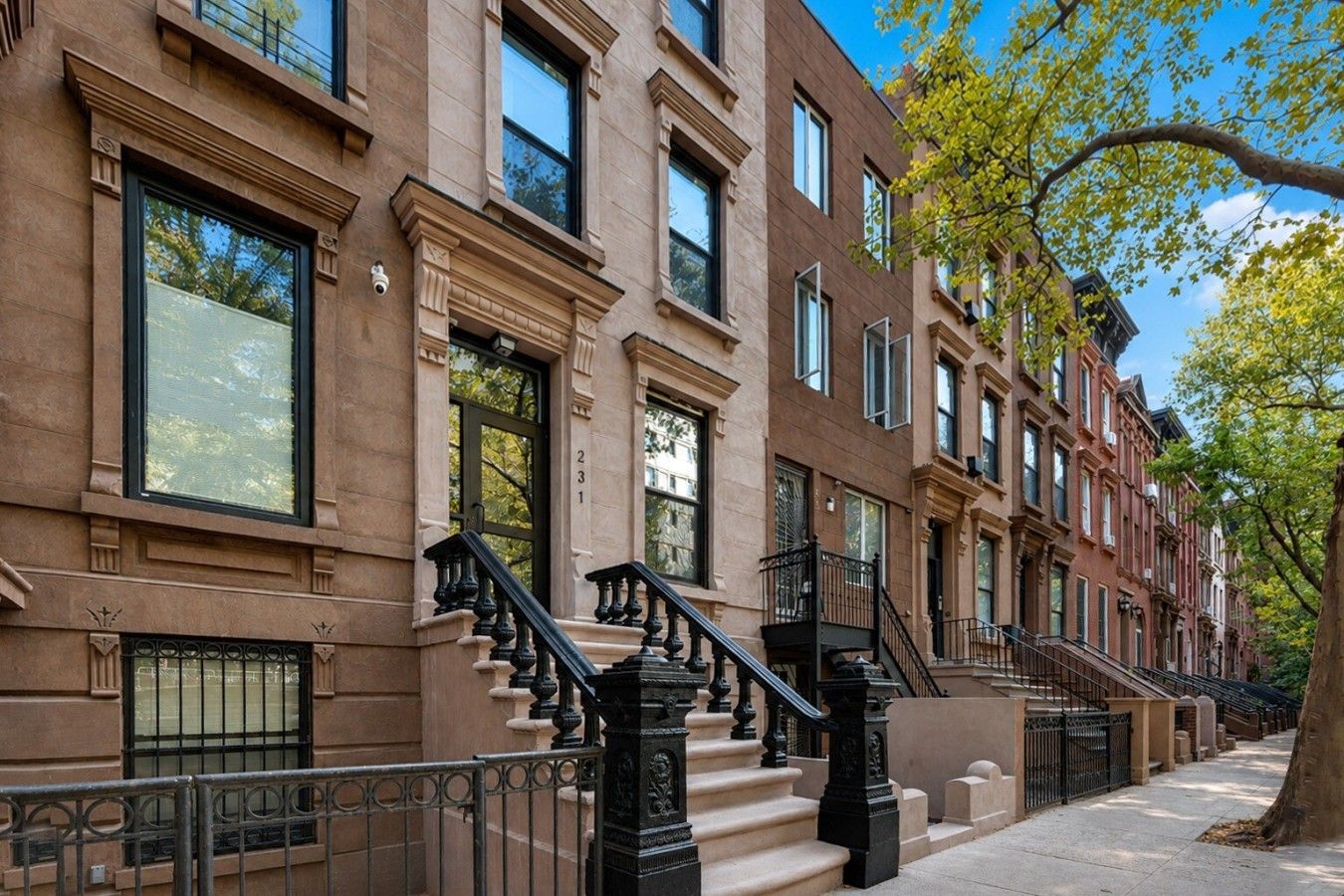 A row of brownstone buildings with uniform architectural style, featuring large windows and black iron railings on the ground floor.
