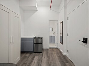 A modern kitchen with grey cabinets, a stainless steel refrigerator, and a wooden floor. - Spacious King Room with Full-Size Sleeper Sofa (New York)