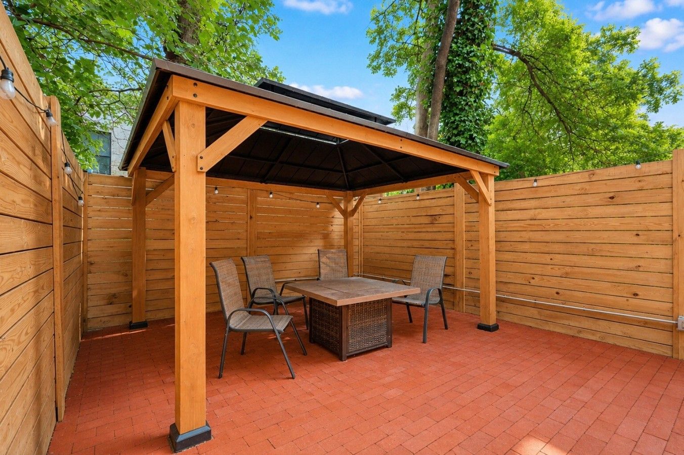 A wooden pergola with a table and chairs, surrounded by a brick patio.