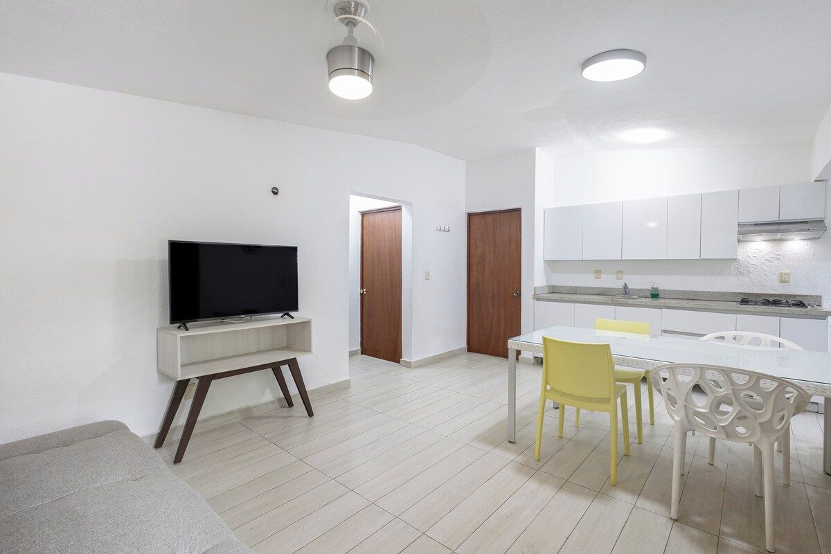 Una sala de estar moderna con un televisor de pantalla plana, un sofá y un comedor con mesa y sillas.