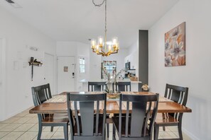 Ein Essbereich mit Holztisch und Stühlen, einer Kronleuchter und einer Küche im Hintergrund.