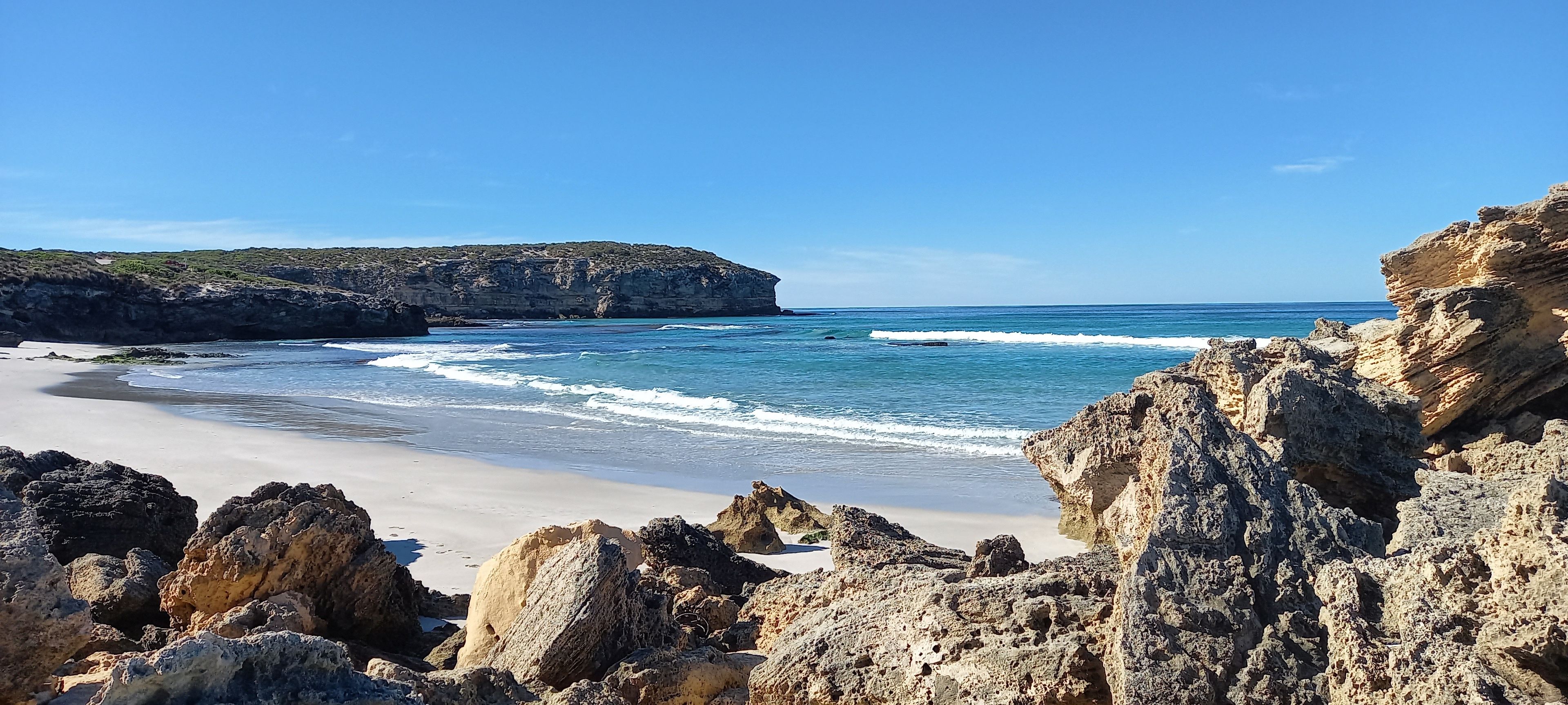 A coastal beach with rocky outcrops and clear blue waters.