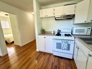 A compact kitchen with white cabinets, a stove, a microwave, and a sink.