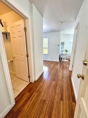 A hallway with wooden flooring, white walls, and a door leading to a room.