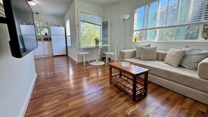 A spacious living area with a wooden floor, a sofa set, a coffee table, and a kitchen in the background.