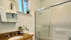 A bathroom with a granite countertop sink, wooden cabinets, a white toilet, and a glass shower enclosure.