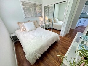 A bedroom with a large bed, bedside tables, a mirror, and a potted plant.