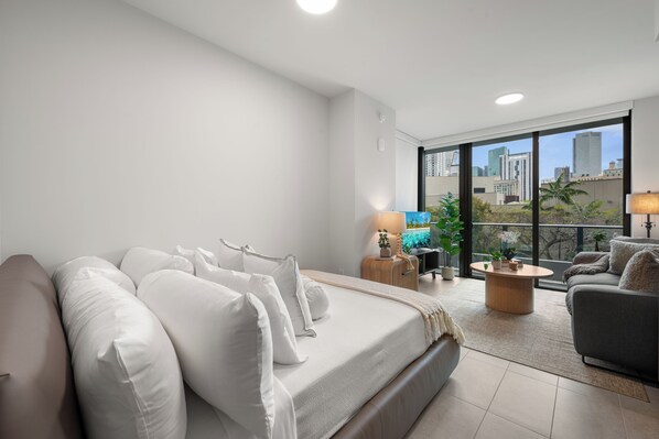 A modern living room with a sofa, a coffee table, and a TV. There is a balcony with a view of the city skyline. - 501 First Studio Balcony by Palermo Home (Miami)