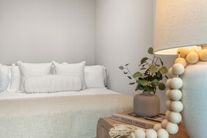 Ein Schlafzimmer mit Bett, Kissen, Nachttisch mit Lampe, einem Buch und einer Pflanze.