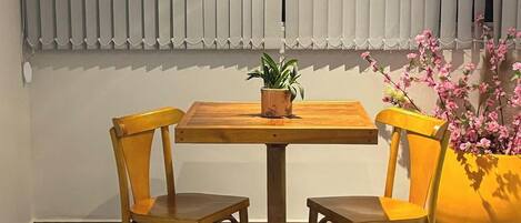 A room with a wooden table and two chairs, a potted plant on the table, and a large yellow planter with pink flowers.