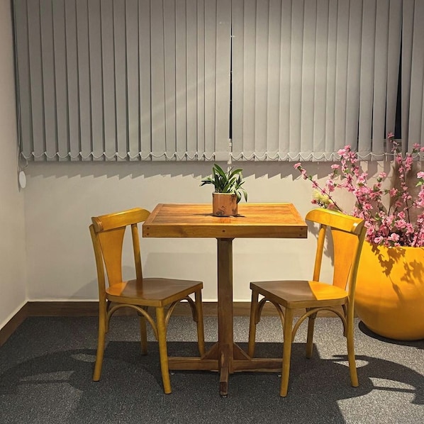 A room with a wooden table and two chairs, a potted plant on the table, and a large yellow planter with pink flowers.