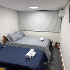 A hotel room with two beds, a large window, a ceiling light, and a wall-mounted air conditioning unit.