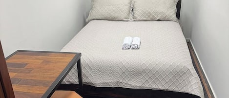 A small, neatly arranged bedroom with a bed, a table, and a chair.