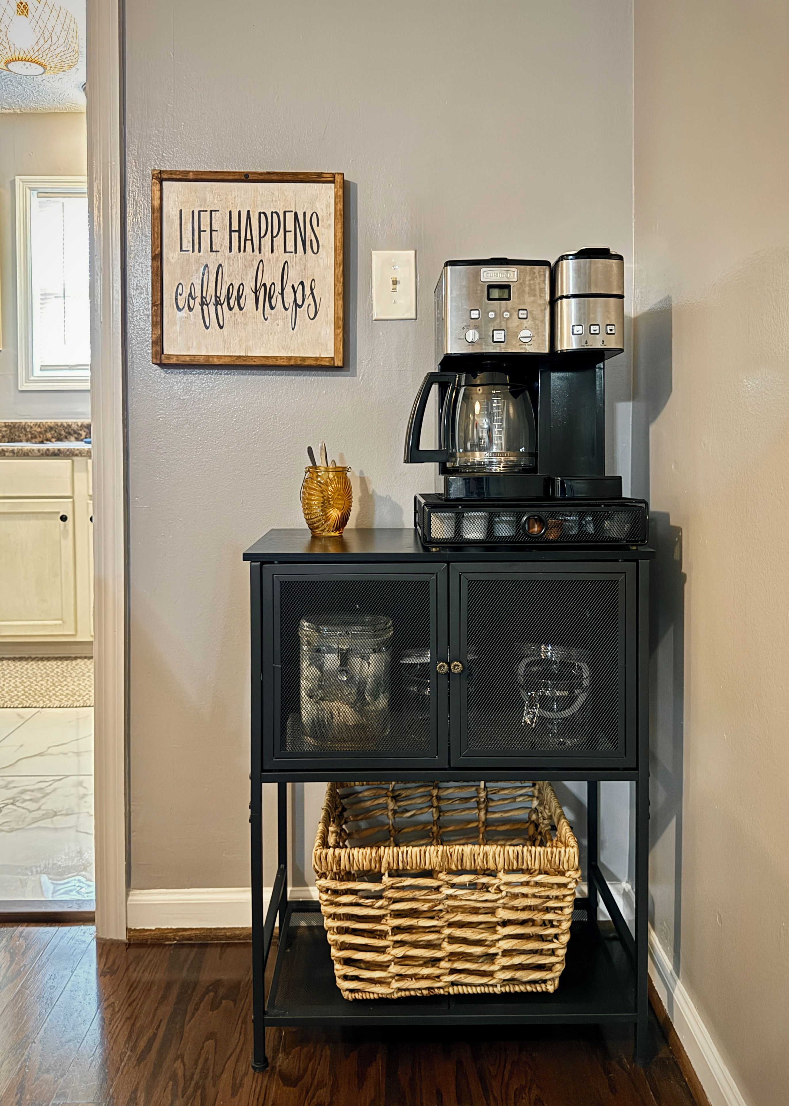 A kitchen with a coffee maker, a cabinet with mesh doors, and a wall sign.