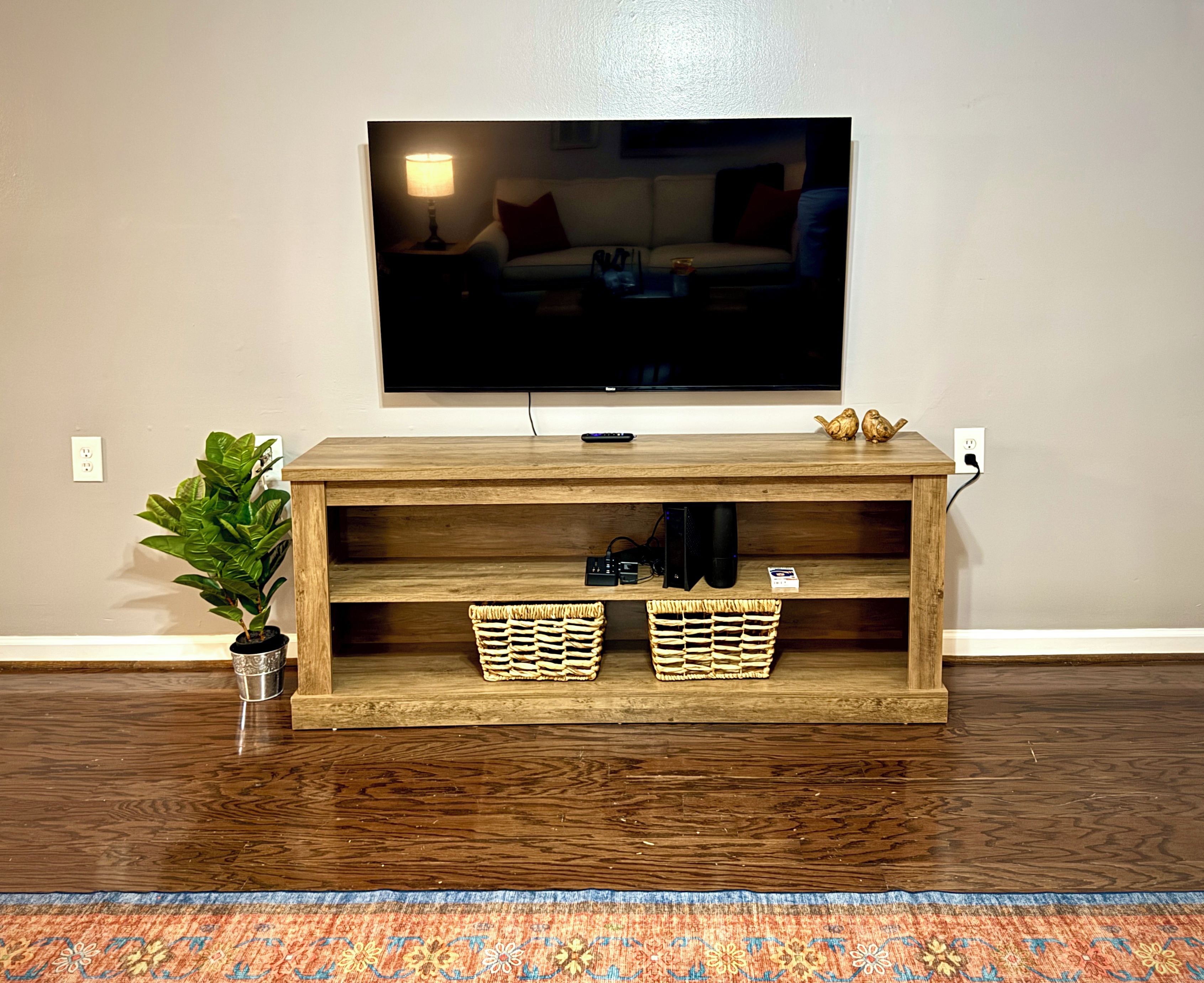 Ein Holzunterhaltungsschrank mit einem flachbildfernseher darüber, zwei Korbwannen auf den unteren Regalen und einer Blumentopf auf der linken Seite.