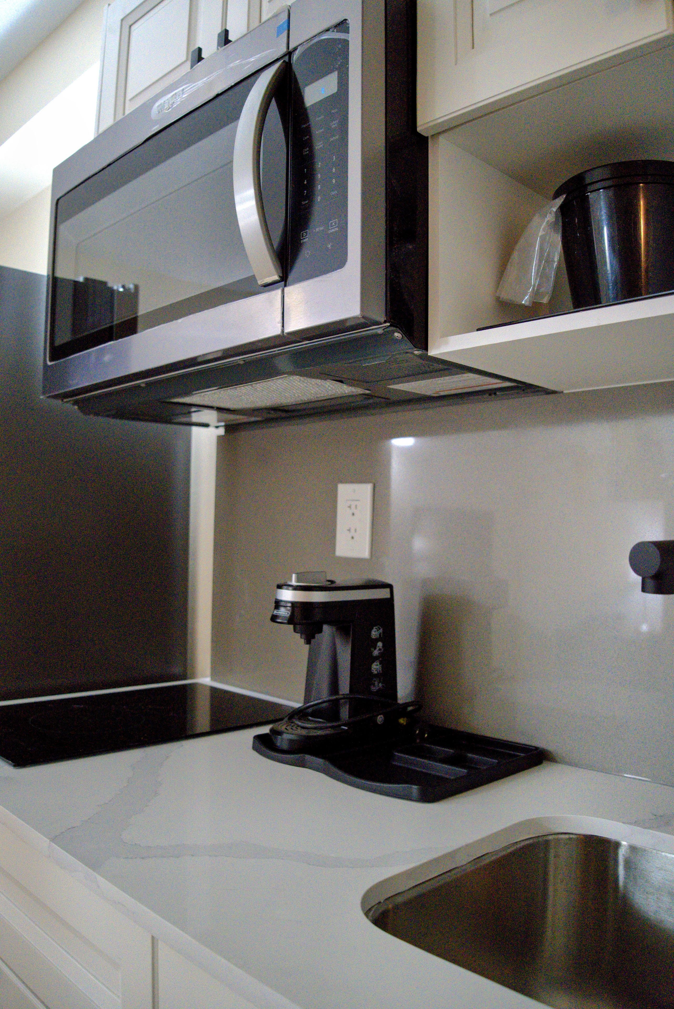 A kitchen with a stainless steel microwave, a coffee maker, and a sink.
