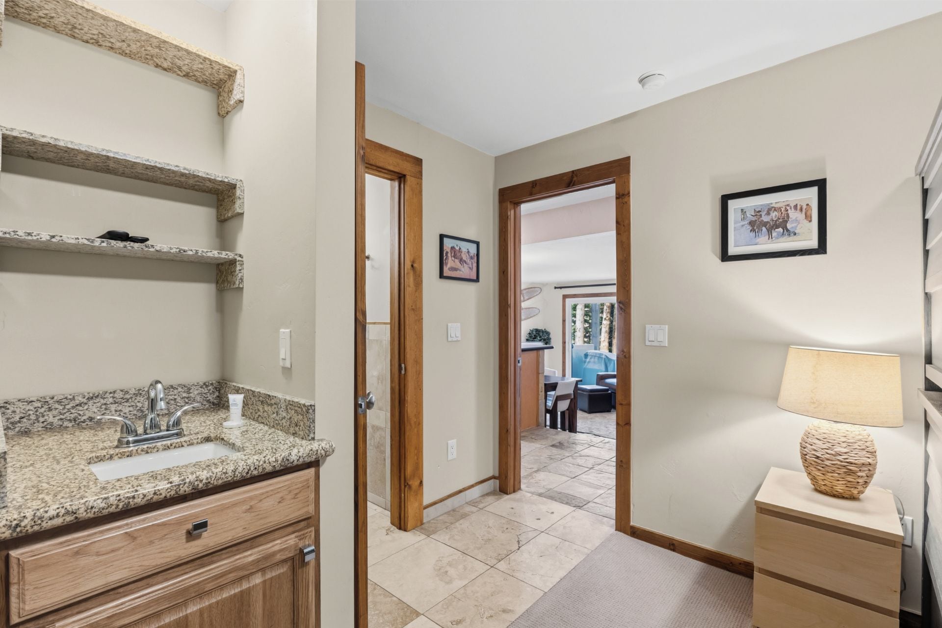 A bathroom with a granite countertop sink, wooden cabinets, and a wooden door leading to a dining area.