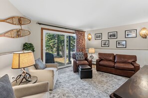 A living room with a sofa, armchair, and a coffee table. There is a large window with a view of trees and a car outside. - *EZCancel* Gold Camp Nugget - Renovated & Walking Distance to Chairlifts (Breckenridge)