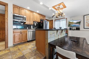 A kitchen with wooden cabinets, a stainless steel refrigerator, a dishwasher, and a dining area with a table and chairs. - *EZCancel* Gold Camp Nugget - Renovated & Walking Distance to Chairlifts (Breckenridge)