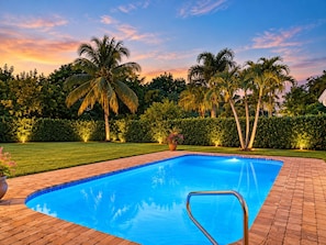 A rectangular swimming pool with a clear blue water surface, surrounded by a brick deck.