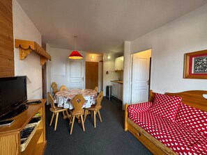 Ein gemütlicher Raum mit Esstisch, Stühlen, einem Bett mit Herzmuster-Bettwäsche, einem Fernseher und einer Küchenzeile.