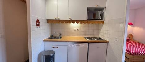 A compact kitchen with white cabinets, a microwave, a sink, and a dishwasher.