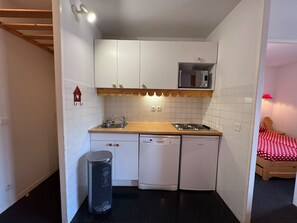 Una cocina compacta con gabinetes blancos, microondas, pileta y lavavajillas.