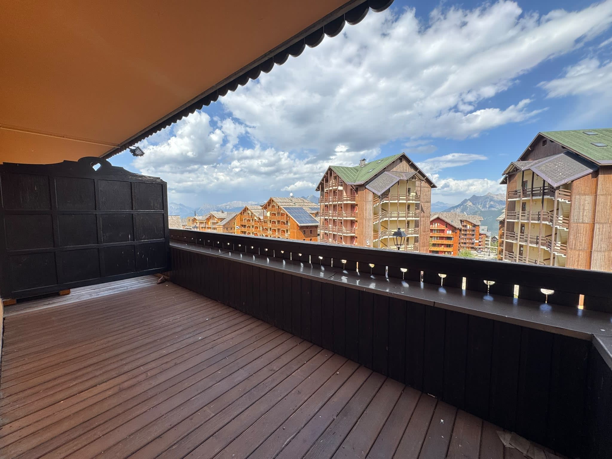 Une terrasse en bois offrant une vue sur des bâtiments de style chalet traditionnel et sur les montagnes en arrière-plan.