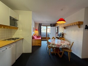 A compact kitchen with a stove, microwave, and dishwasher. There is a dining area with a table and chairs, and a small seating area with a sofa. - T4 6 personnes avec grand balcon • piscine & sauna • Risoul (Risoul)