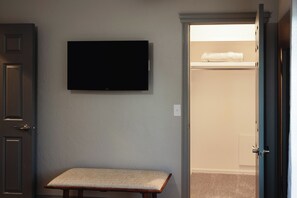 Ein Zimmer mit einem wandmontierten Flachbildfernseher, einer Bank und einer Tür zu einem Schrank mit einem Handtuch darauf.