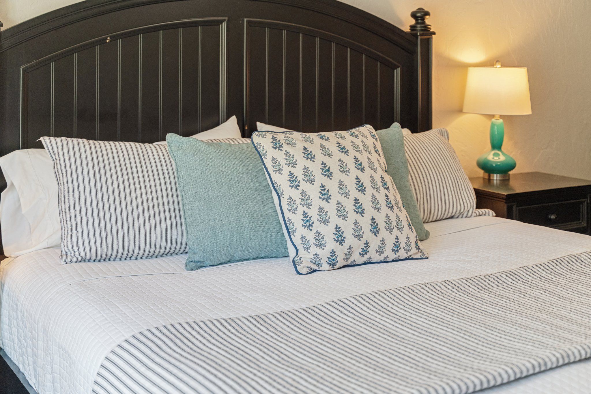 A bed with a striped bedspread and multiple pillows, a dark headboard, and a nightstand with a lamp.